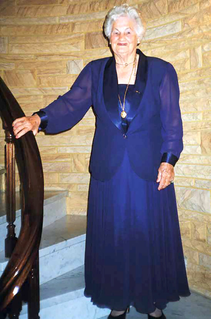 Photograph of Pearl Batchelor OAM standing on stairway wearing an evening gown